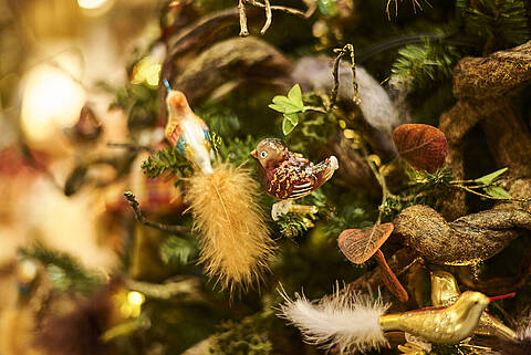 Detailreiche Vogelanhänger mit Federn als Christbaumschmuck im JOSKA Weihnachtsland, festlich arrangiert am Baum.