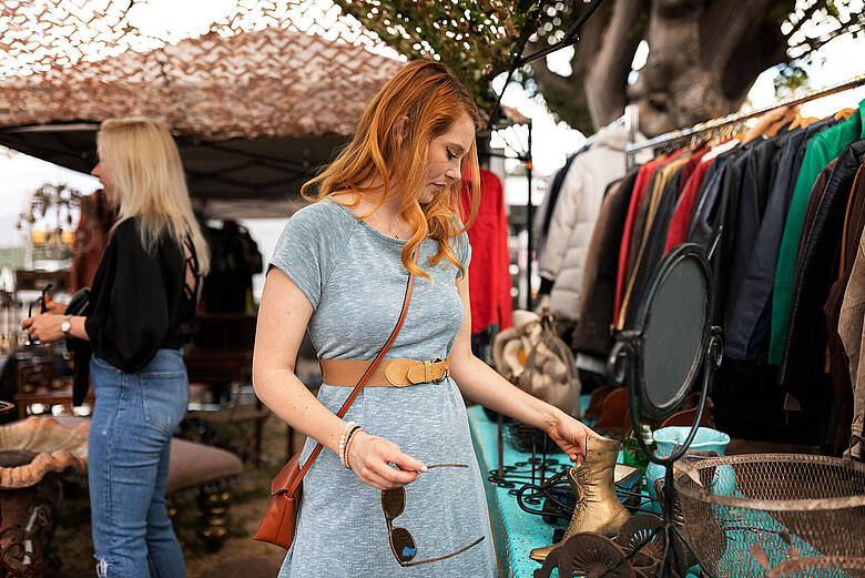 Frau stöbert beim Mädelsflohmarkt durch Second-Hand-Kleidung und Accessoires