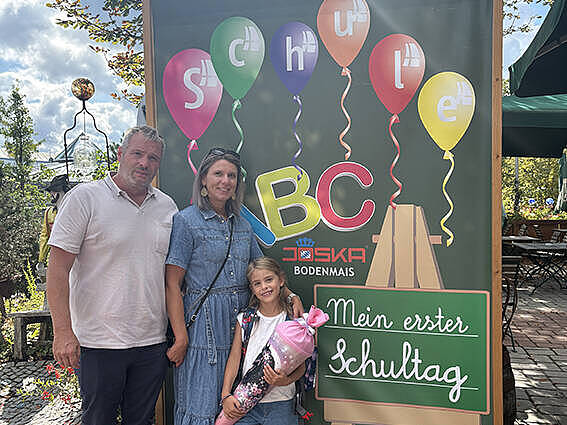 Schulanfängerin mit Schultüte und ihrer Familie vor der Fotowand „Mein erster Schultag“ im JOSKA Glasparadies in Bodenmais.