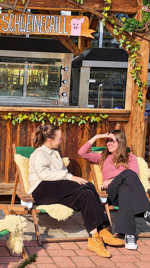Zwei Frauen genießen die Sonne in gemütlichen Liegestühlen mit kuscheligen Fellen vor dem Schweinegrill im JOSKA Glasparadies in Bodenmais.