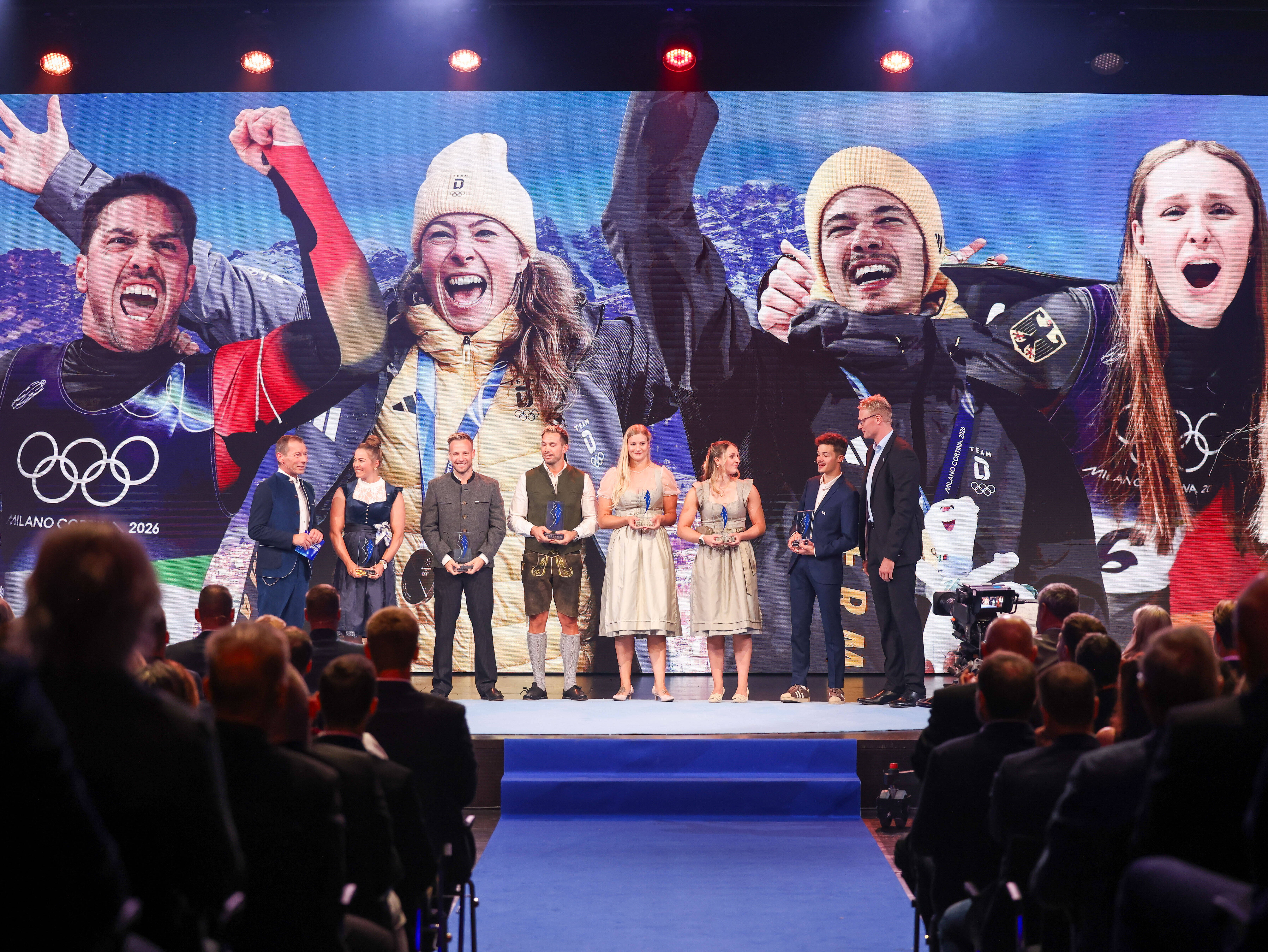 Preisträgerinnen und Preisträger bei der Verleihung des Bayerischen Sportpreises 2026 auf der Bühne vor einer großen Videowand mit Sportmotiven.