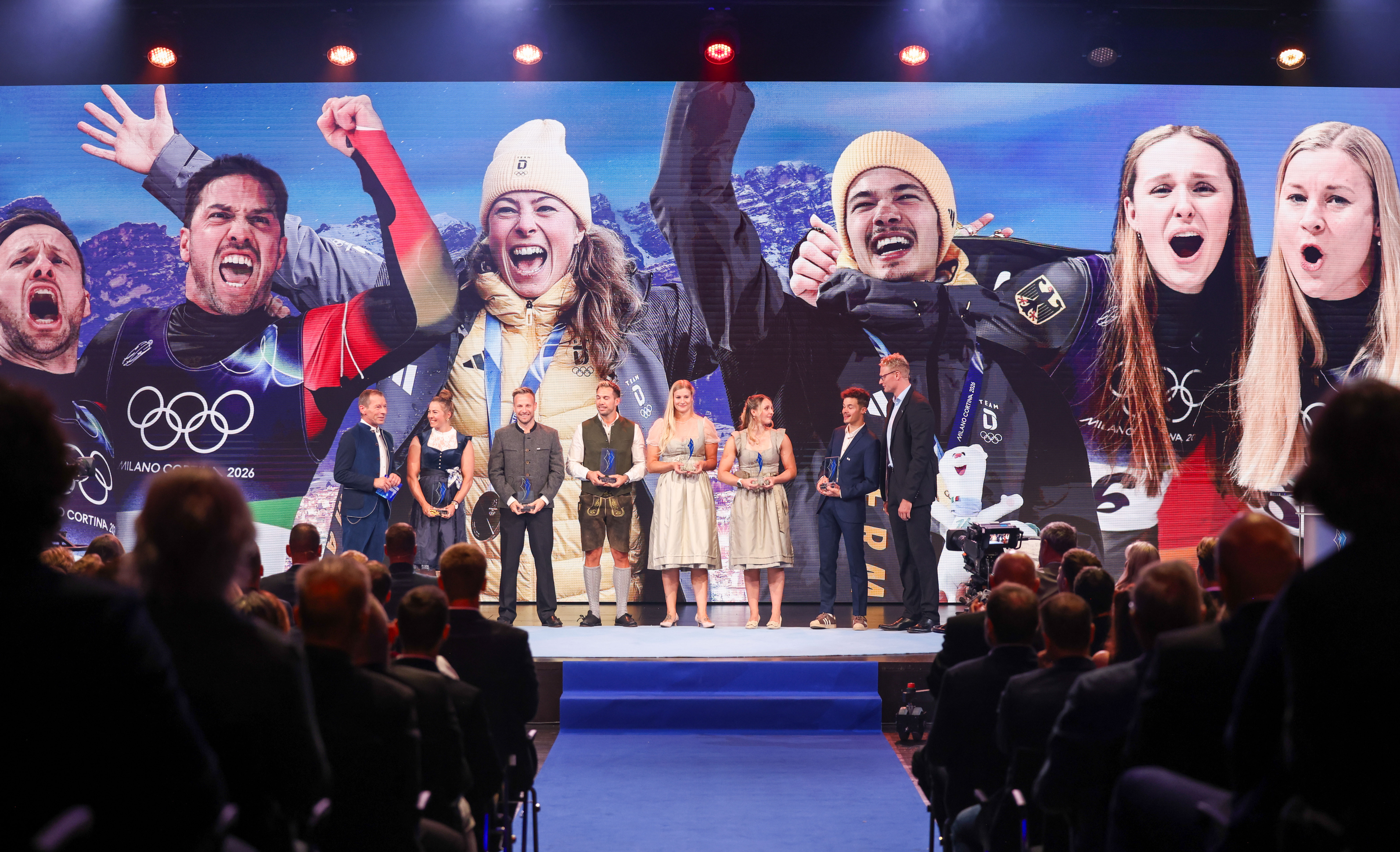 Preisträgerinnen und Preisträger bei der Verleihung des Bayerischen Sportpreises 2026 auf der Bühne vor einer großen Videowand mit Sportmotiven.